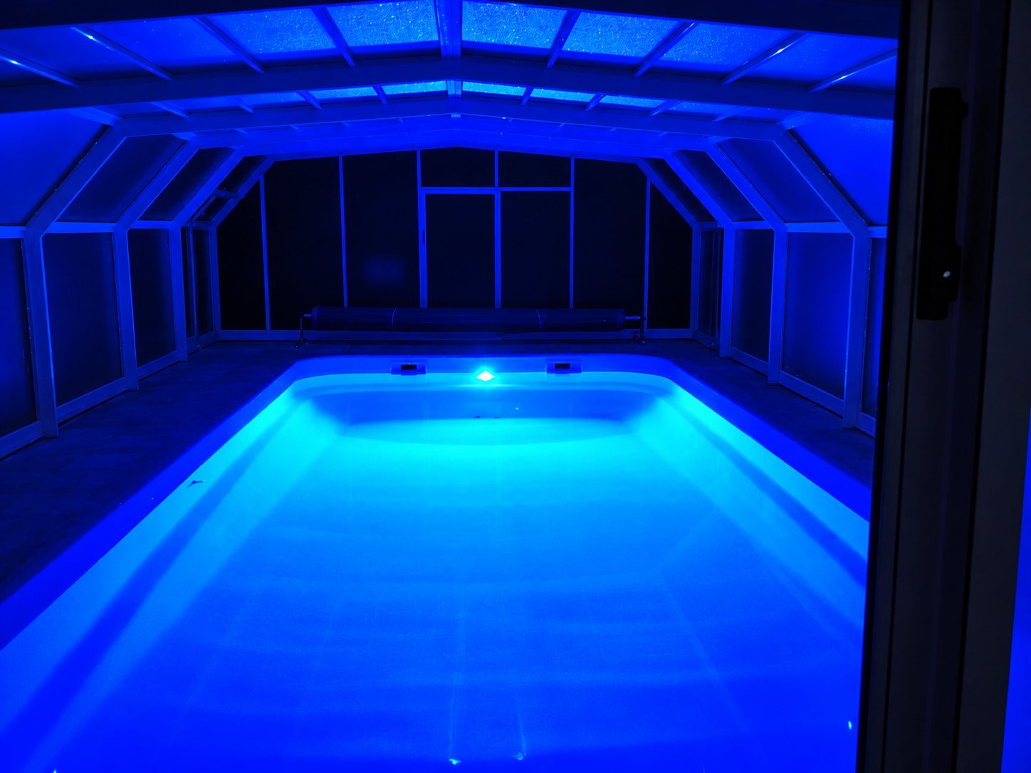 Une piscine rectangulaire éclairée par des LED bleues à l'intérieur d'un abri vitré plongé dans l'obscurité.